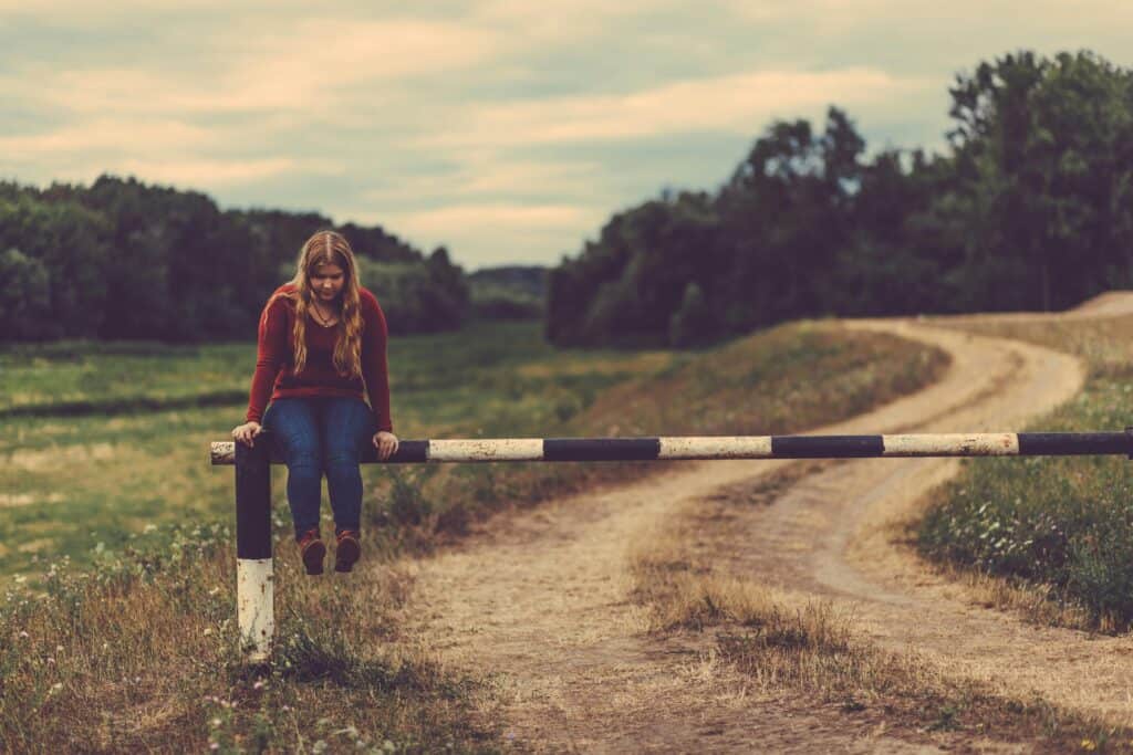 girl sitting on a guard rail in the country sad