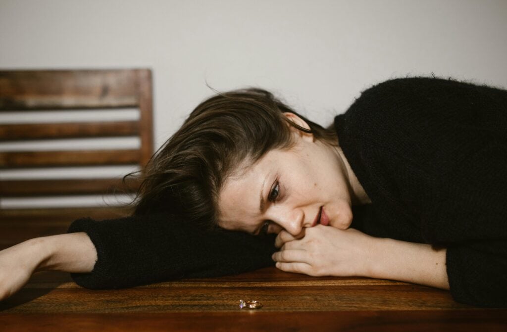 woman head on the table crying looking at wedding ring