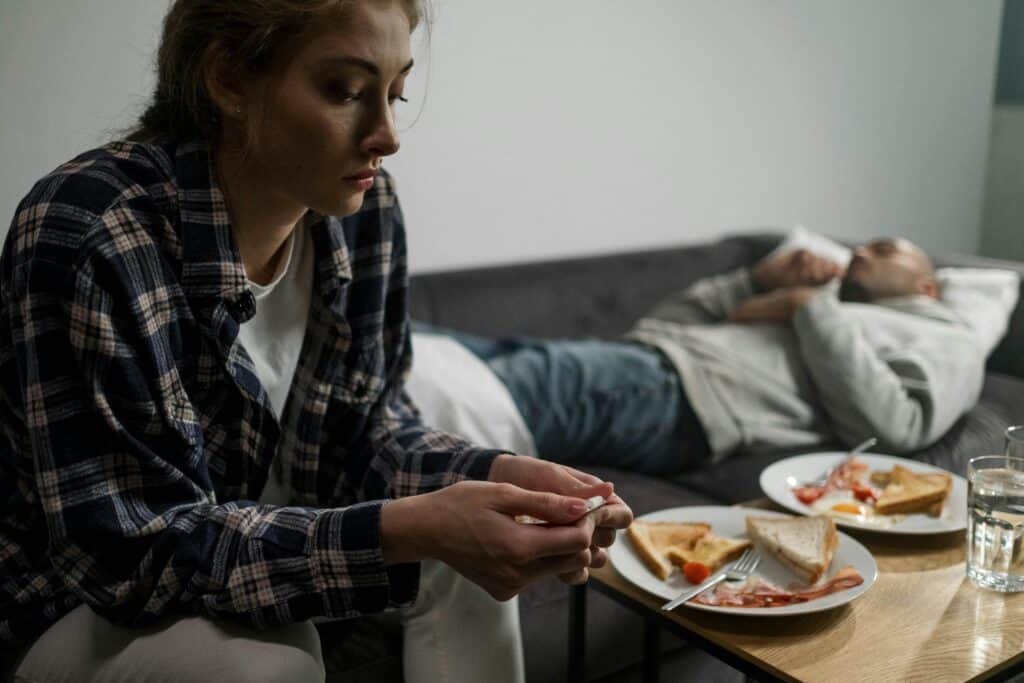 woman sitting in front of half eaten breakfast man sleeping in background