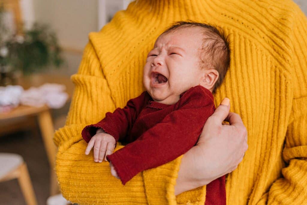 baby in woman's arms mouth open angry cry