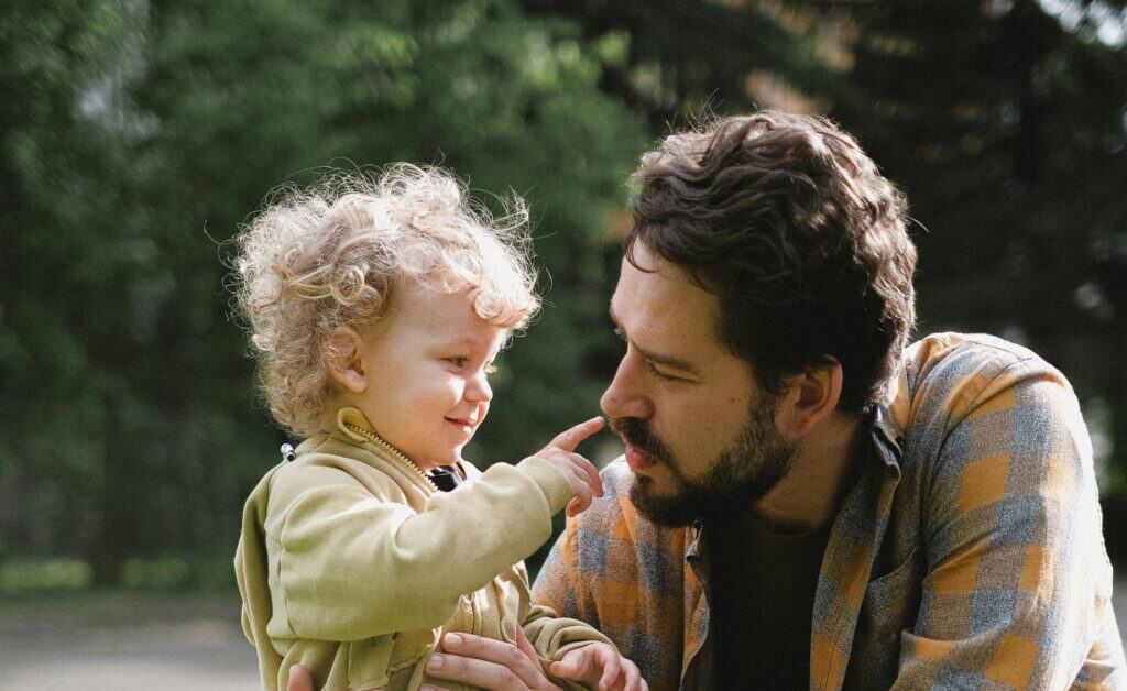 small child pointing at man's nose