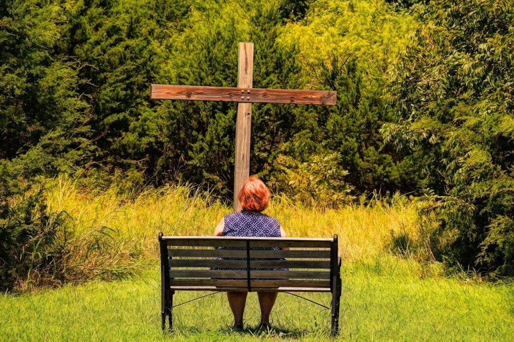 woman on bench looking at large wooden cross