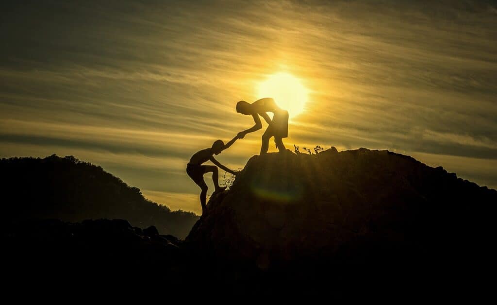 one person helping another up a hill at sunset