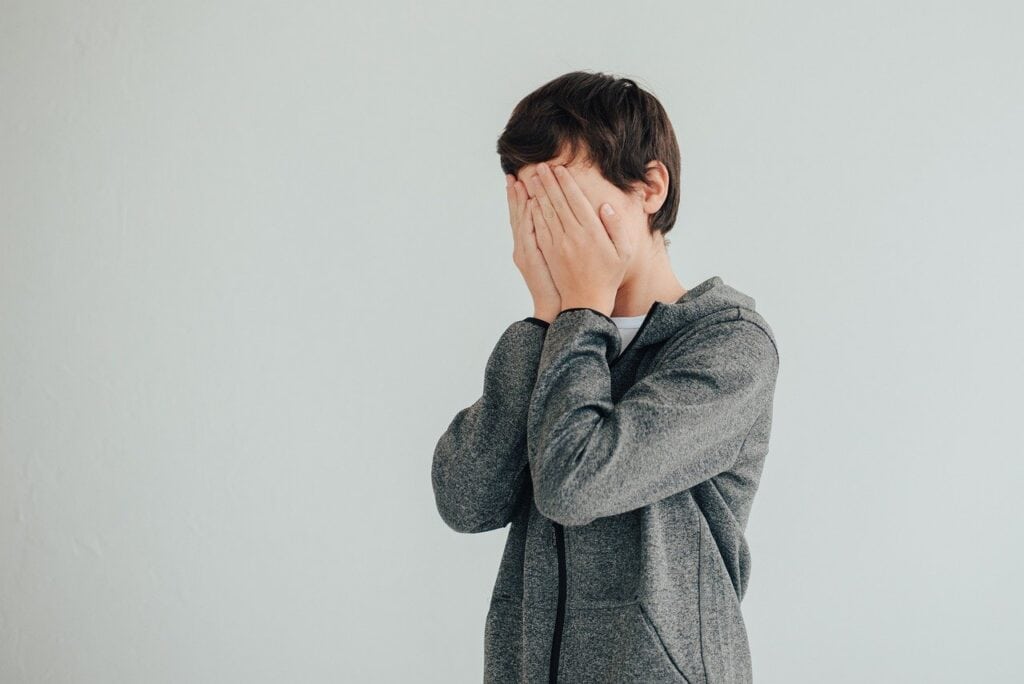 teen boy covering face with hands