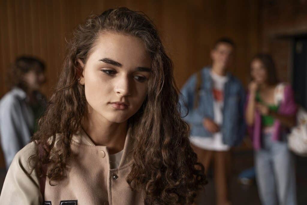 girl frowning while other teens talk about her in the background
