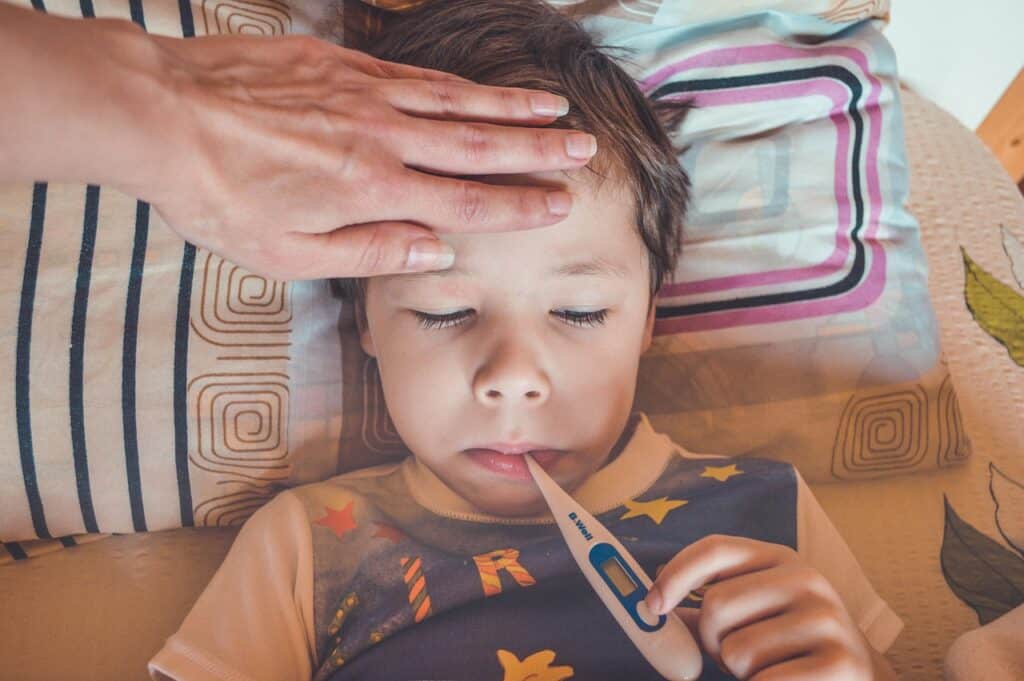 little boy in bed with thermometer adult hand on his head