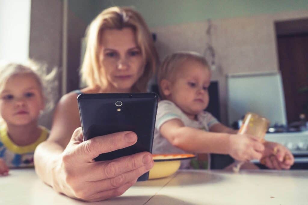 mom on phone flanked by two young kids