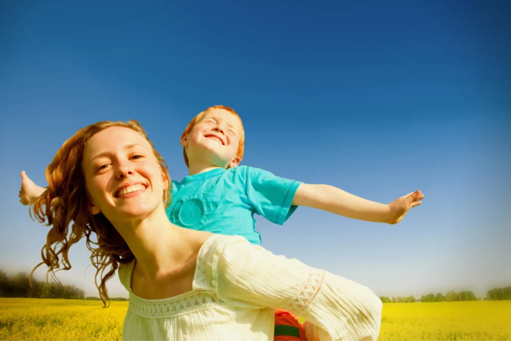 Smiling single mom carrying happy child in a field, showing grit and joy in parenting.