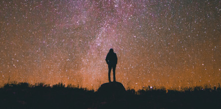 Silhouette of person standing on a hill looking into a beautiful night sky that's full of stars