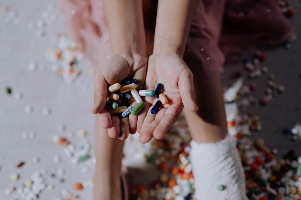 child's hands holding various pills drugs