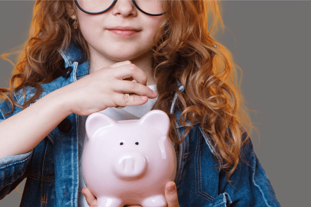 Close up picture of a red headed little girl holding a piggy bank putting money in