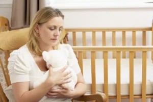 A grieving woman sitting in a nursery, holding a white teddy bear, symbolizing the emotional journey of coping with miscarriage.