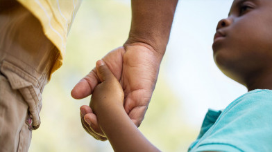 Close up of a father's hand holding his young son's as his son looks up at him