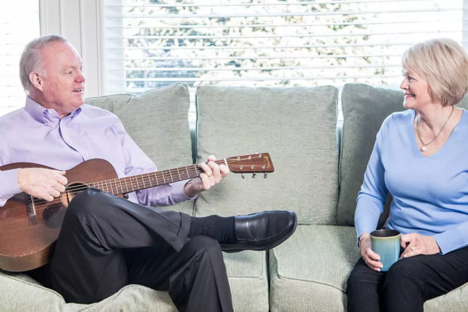 Bo and Gari Mitchell sitting on the couch in their home while Gary plays the guitar, showing that God's grace while Bo Mitchell was behind bar helped restore their marriage.