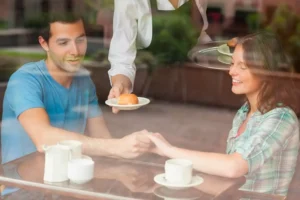 A couple sits in a café, holding hands and smiling, highlighting the importance of communication in marriage and how it can be an example of Christ's love for us.