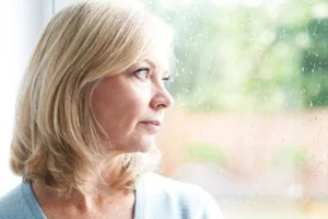 A woman gazing out of a rain-streaked window, symbolizing the connection between depression and emotion through a reflective and somber moment.