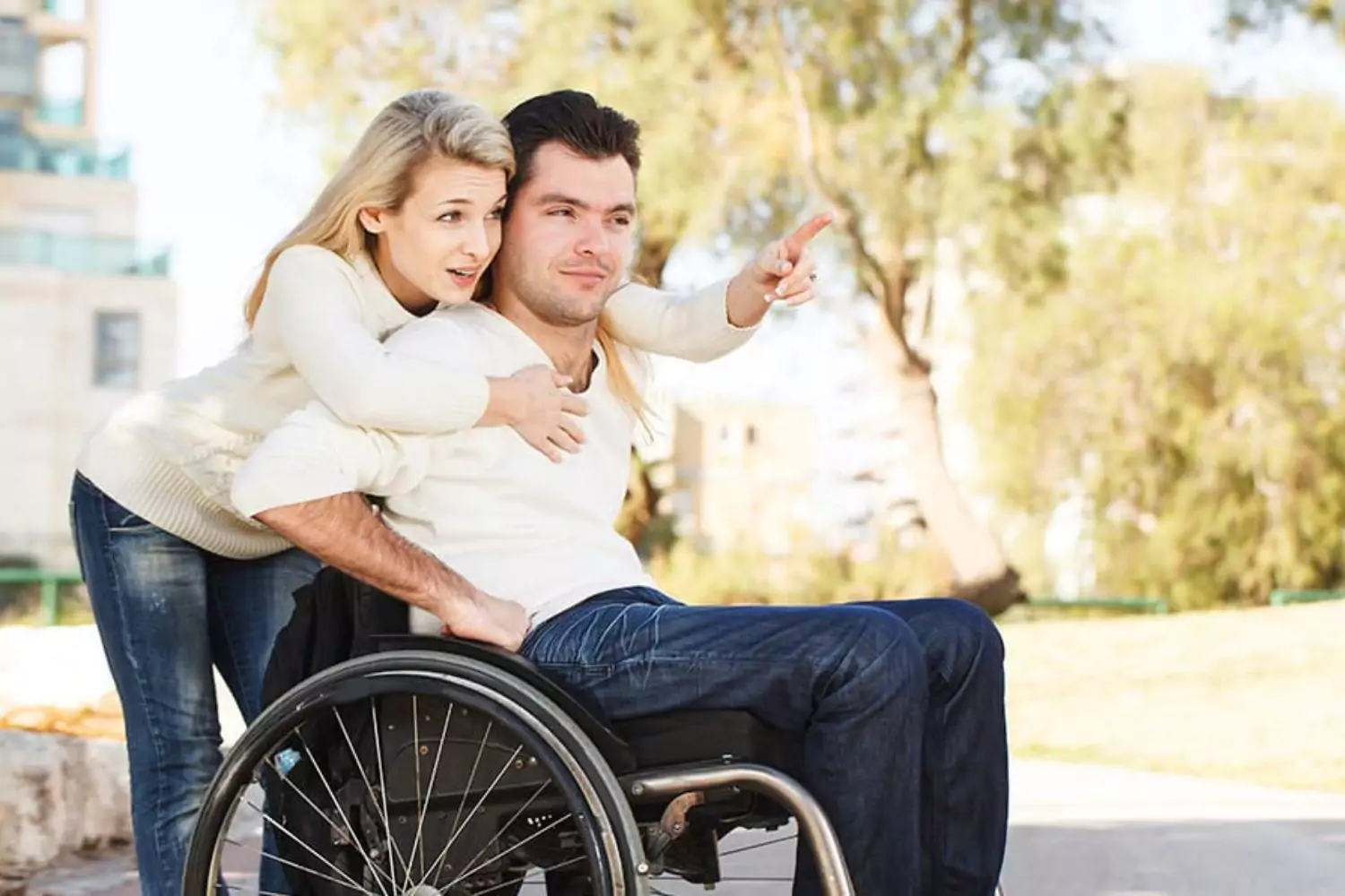 A woman embraces a man in a wheelchair, both wearing expressions of hope and positivity despite the challenges of facing a terminal illness.