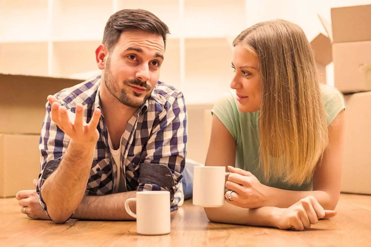 A couple lying on the floor with coffee mugs, engaged in a relaxed yet thoughtful conversation, reflecting the openness required for discussions like, “Let’s talk about sex.”