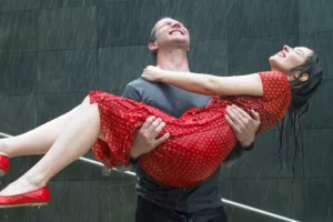 A romantic scene of a man joyfully holding a woman in his arms as they embrace the rain, symbolizing a heartfelt moment in a romance story, and how you can make that same romance come alive in your marriage.