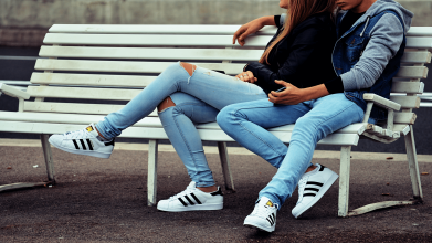 Young couple sitting outside on a bench, dressed similarly with blue jeans and matching sneakers.