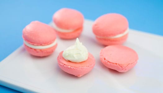 Pink, puffy sandwich cookies with white creme filling in the middle against a blue backdrop