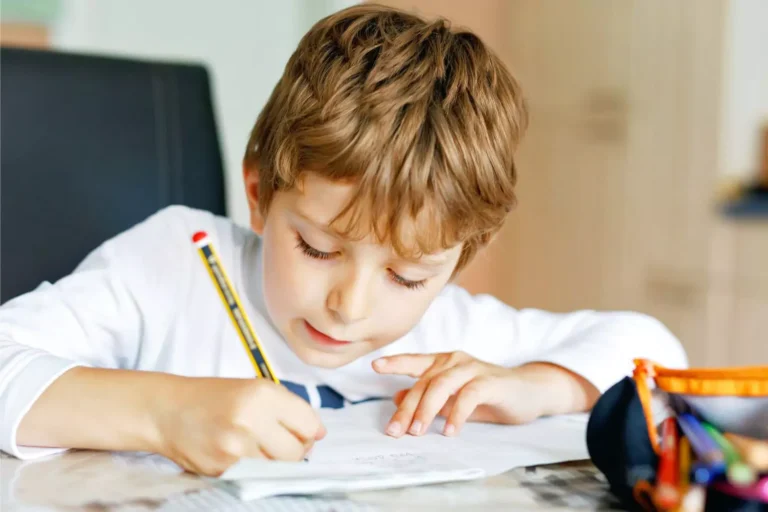 Homeschooling little boy sitting at a table writing with a pencil.