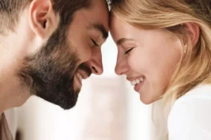 A joyful couple leans their foreheads together with eyes closed and smiles on their faces, symbolizing spiritual unity in marriage.