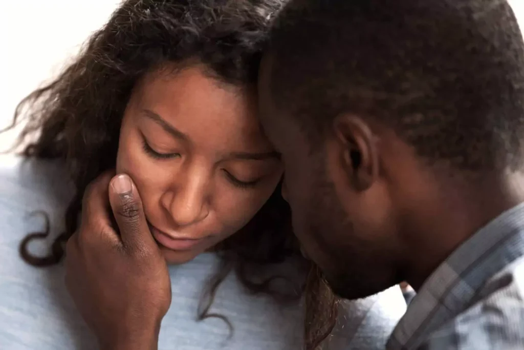 A grieving couple shares an intimate moment, with the man gently holding the woman’s face as she closes her eyes, symbolizing one of the many ways to love your spouse after a miscarriage.