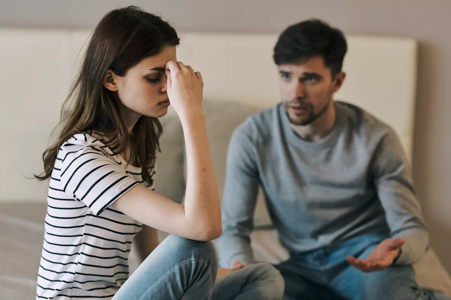 A woman sits on the edge of the bed with her head in her hand, as if stressed out. Her husband sits on the other end, trying to talk to her. Here are some tips to deal with past abortions in marriage.