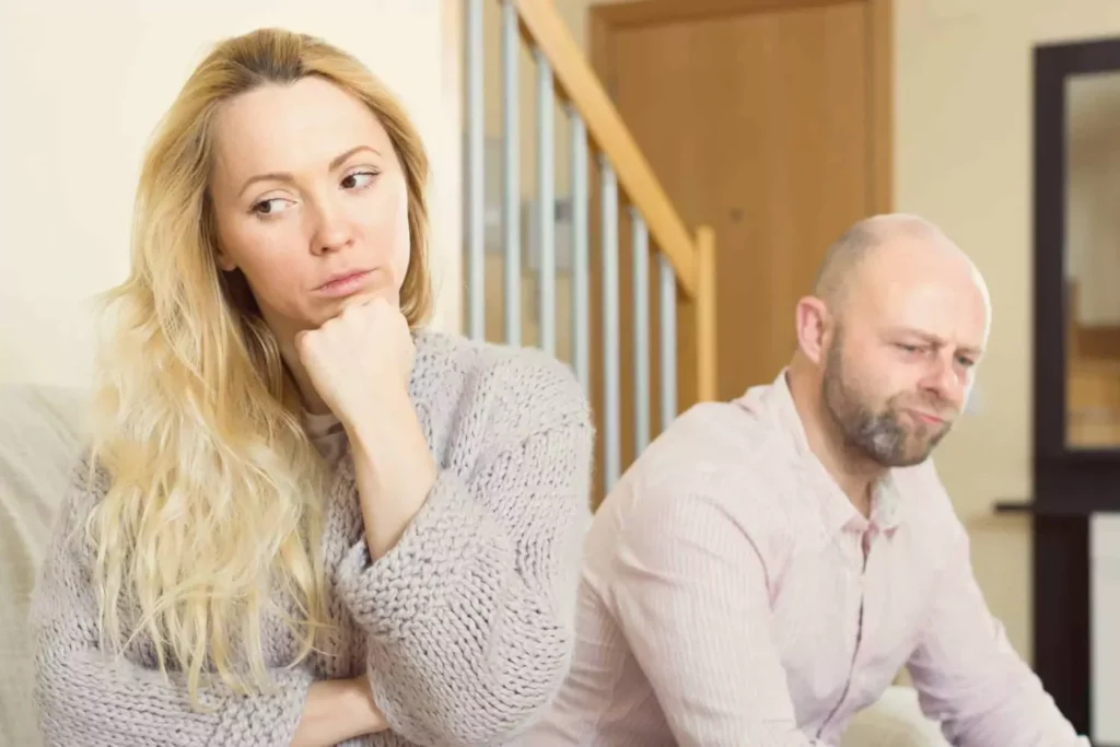 Upset couple sitting on their couch. Her back is turned to him as she tries to rebuild trust after he has shared personal information with other people. They're both in deep thought.