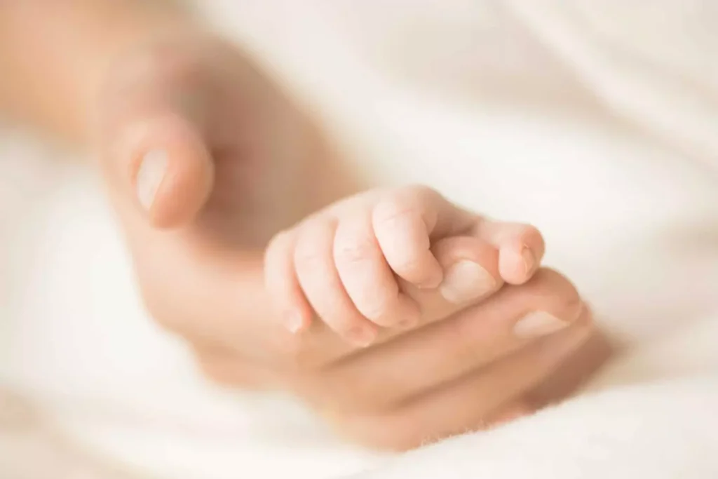 A delicate image of a baby’s tiny hand gently resting in an adult’s open palm, symbolizing love, protection, and loss. The soft, blurred background creates a serene and emotional atmosphere, evoking the deep sorrow and heartbreak associated with the loss of a child.