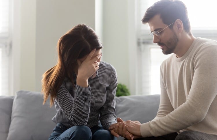 Husband comforting his crying wife as they sit on their couch