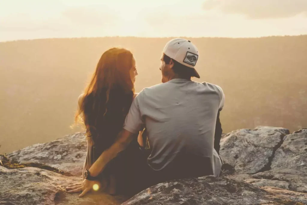 A couple sits on a rocky overlook at sunset, gazing into each other’s eyes, symbolizing how to improve communication skills with your spouse through word pictures.