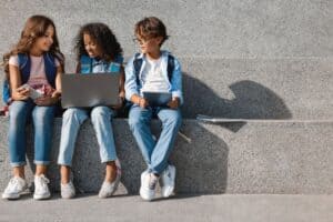 Three teen girls sitting on an outdoor step looking at laptops