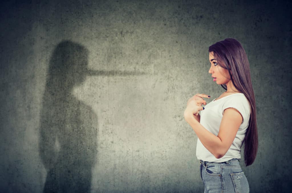 A young pro-life woman looks at a shadow of herself with a long nose indicating hypocrisy.