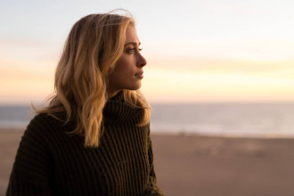 Young, serious-looking woman standing on a beach looking out at the ocean