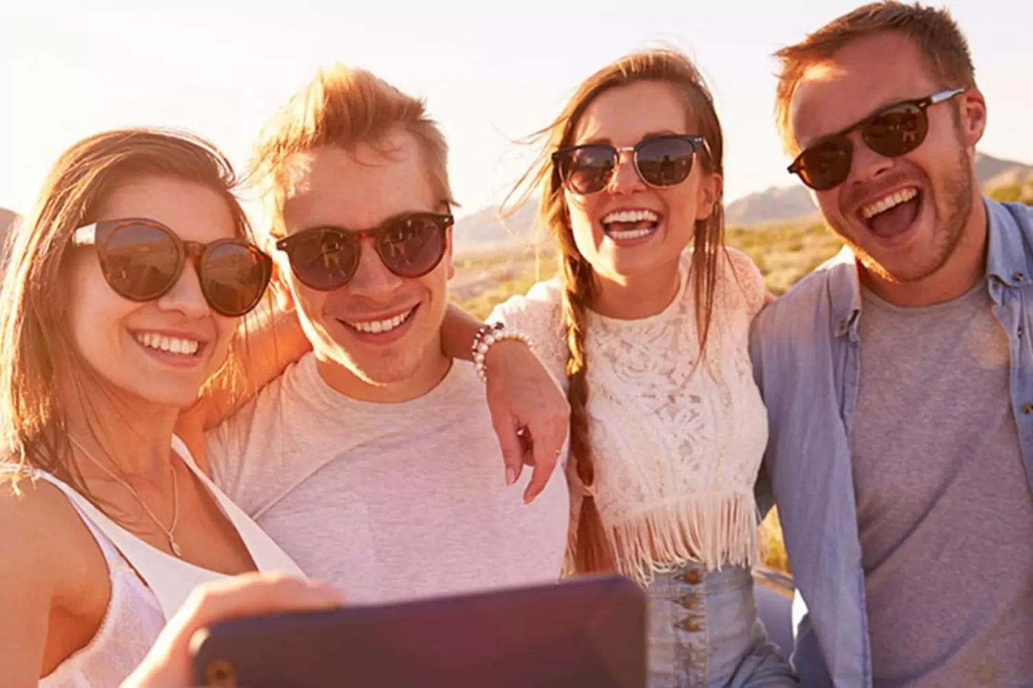 Four friends, two men and two women, smiling and taking a selfie together. They sometimes wonder about the Bible's stance on if men and women can be friends.