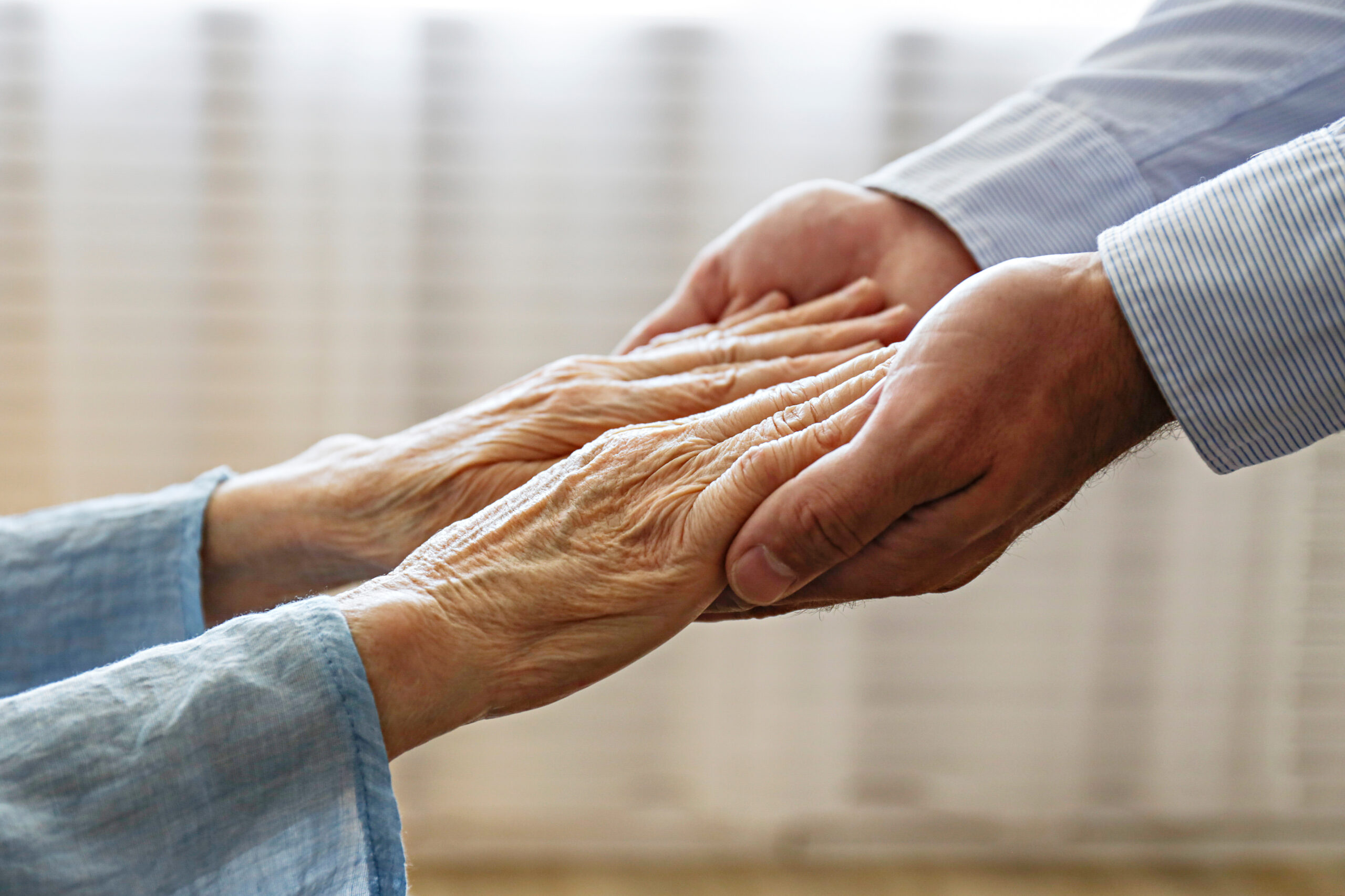 Close up of aged wrinkled hands of senior woman reaching to a male doctor.