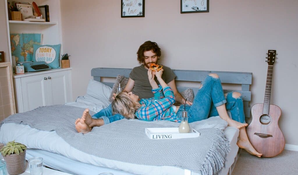 Man and woman lying on bed eating pizza