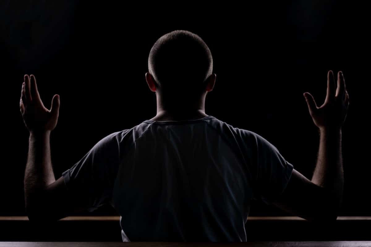 Photo of a man praying in the dark, hands lifted in the air.