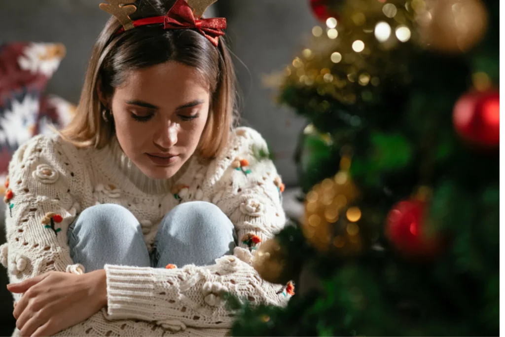 young mother sitting next to a Christmas Tree holding her knees Grieving