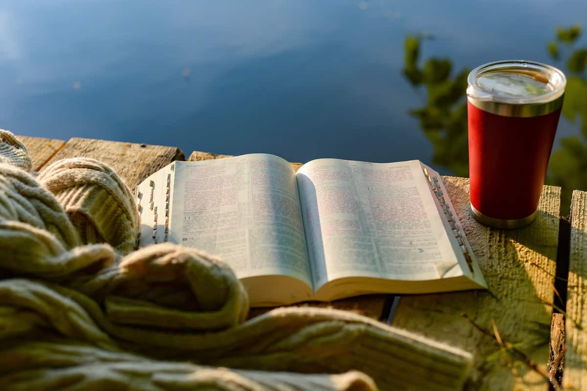 Photo of an open bible and a coffee on a table in the sunlight.