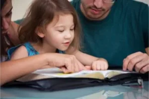 Young girl reading the Bible with her parents