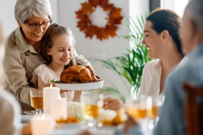 Family gathered around the table to celebrate thanksgiving. Grandma helping her 12 year old granddaughter put dinner on the table.