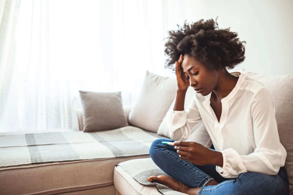 Concerned woman sitting on couch looking at pregnancy test