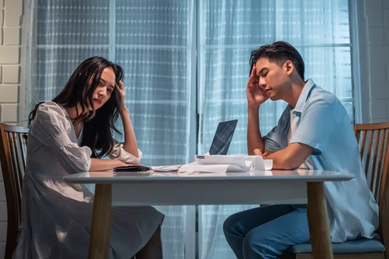 A young couple sits at a table, stressed out over finances. Financial abuse in marriage is a real problem.