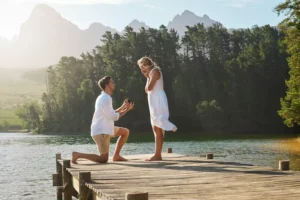A young man proposes to a woman on a dock on a lake in the mountains. Are you ready to wed?