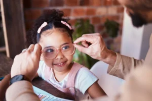 Will homeschooling make my kid weird? Pretty little girl with pick barraretts in her hair, with her dad putting her pink glasses on her as she smiles.
