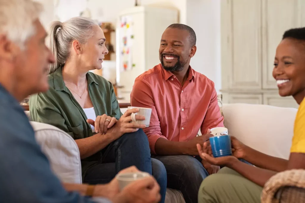 A young couple sits with a mature couple in fellowship around a couch. Marriage mentoring can be important in helping young couples navigate the issues they will face together. Here are five ways to find a mentor couple.