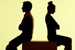 A man and a woman, in silhouette, sit on a box, backs to each other, arms folded. In these divided time, navigating political issue in marriage is important to maintaining relationships.